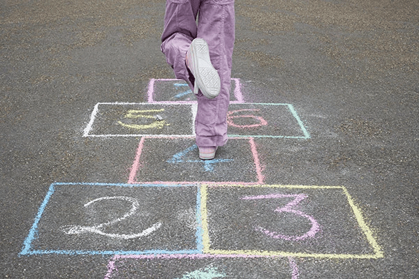 Close-up of child playing hopscotch.