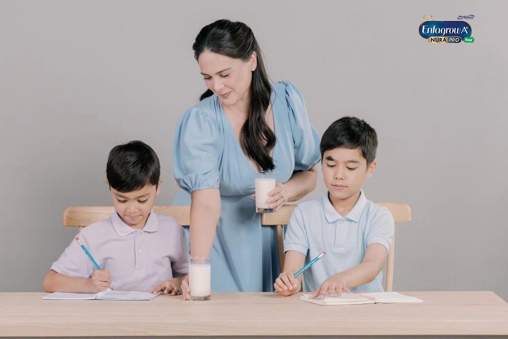 Woman With Two Boys Writing At Table, Each With A Glass Of Milk; 'Enfagrow A+ Nura Pro Four' Logo In Corner