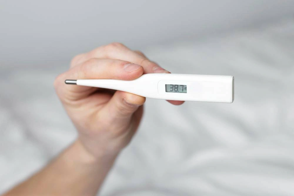 Person Holding A White Digital Thermometer Displaying 38.7