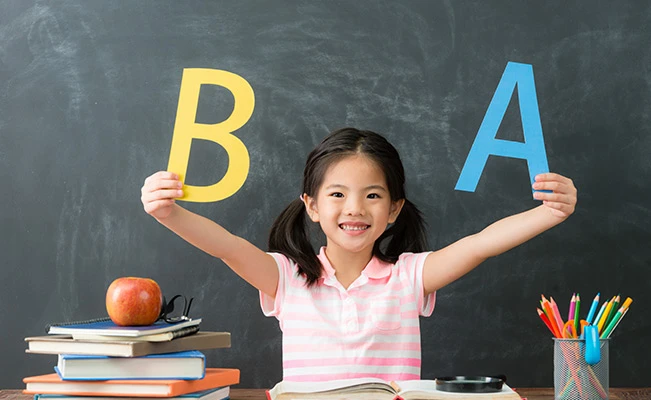 Young preschooler girl holding A and B letters in classroom setting.