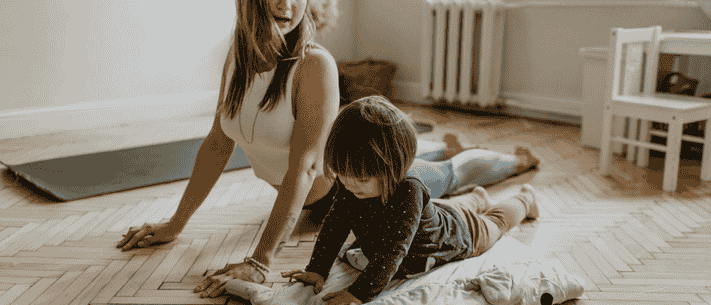 Woman and Child in Cobra Pose on Herringbone Wood Floor, with Yoga Mat Nearby