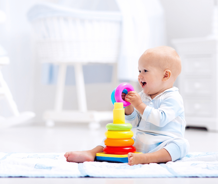 Bebé jugando con torre de aros de colores, desarrollo de habilidades motrices entre 1 y 2 años.