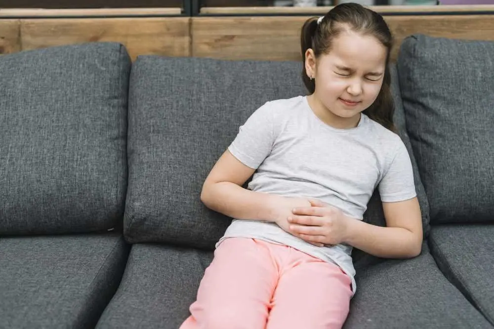Child Sitting In Couch Having Stomach Discomfort 