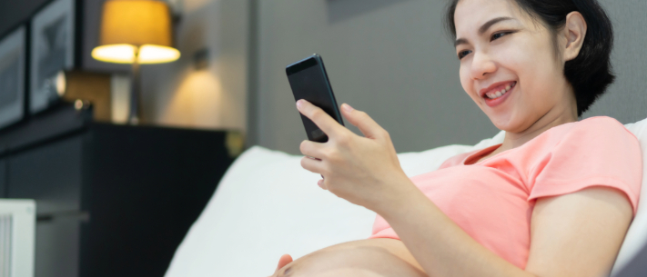 Pregnant woman smiling while looking at phone sitting in sofa