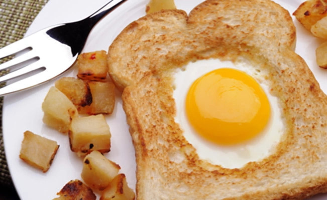 Egg in the nest dish on white platter with potato cubes and fork