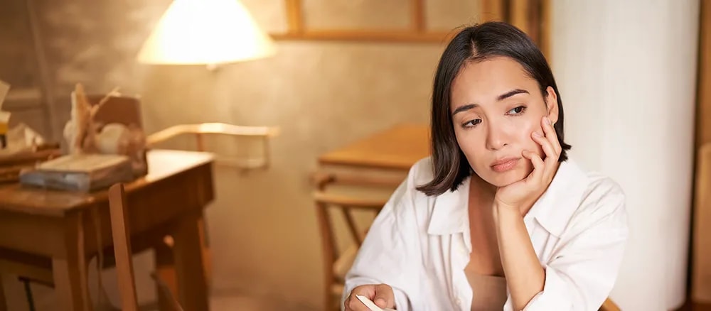 Woman looking thoughtful, resting chin on hand.