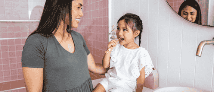 Young Girl Brushing Teeth with Her Mom in Bathroom with Pink Tiled Walls