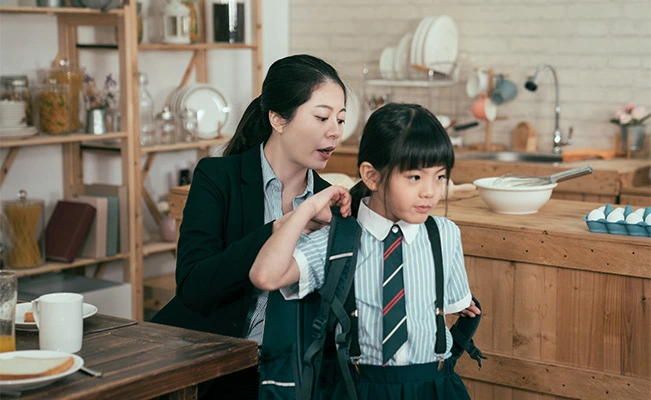 Mother Helping Daughter With School Backpack In Kitchen During Morning Routine 