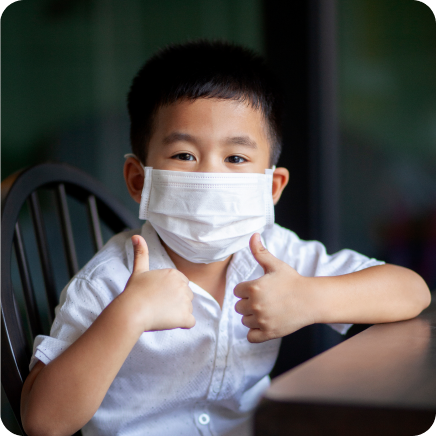 Preschool Boy Wearing A Face Mask And Holding Two Thumbs Up
