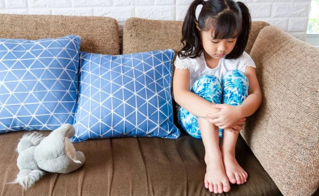 Child Sitting In Couch Having Stomach Discomfort