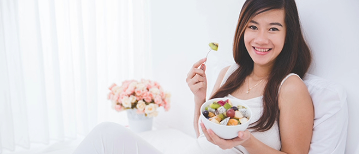 Woman sitting on bed while enjoying a bow of fruits