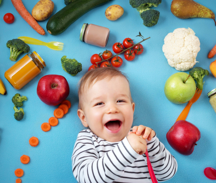 Bebé sonriente rodeado de frutas y verduras frescas, acompañado de texto sobre la introducción de alimentos sólidos en la dieta infantil.