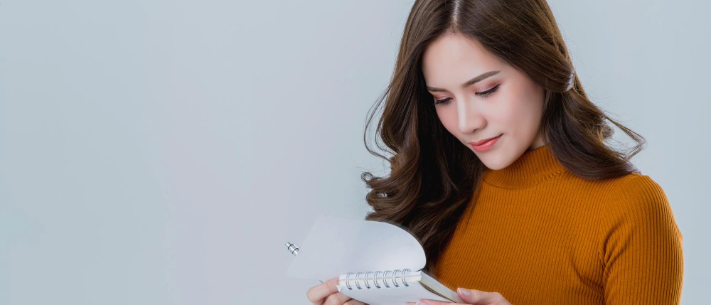 Woman looking at notepad against plain background