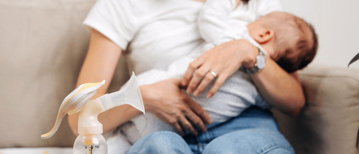Person on Couch Holding Baby with Breast Pump Nearby