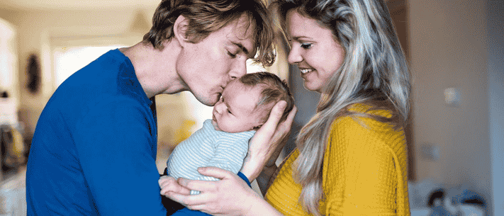 Family of Three with Father Kissing Baby's Forehead and Mother Smiling, Creating a Warm, Intimate Atmosphere