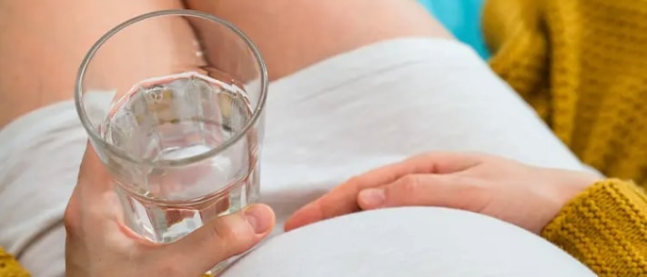 Top view of pregnant woman holding a glass of water
