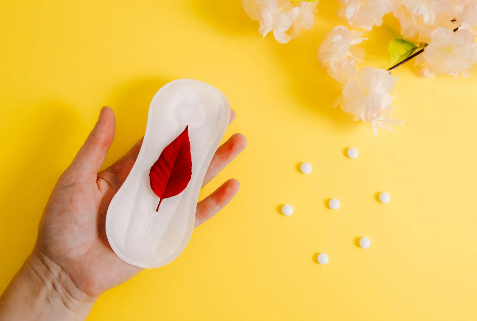 Woman's hand holding sanitary pad with red leaf representing menstruation.