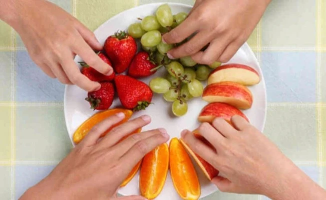 Hands reaching for a plate of fruit