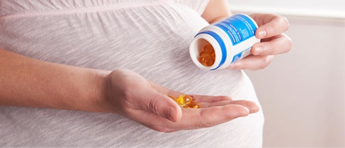 Pregnant woman taking supplements from bottle.