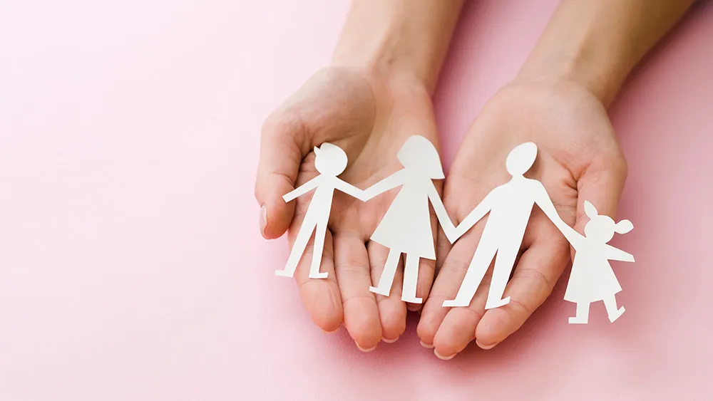 Hands holding paper cutout chain of family figures on pink background