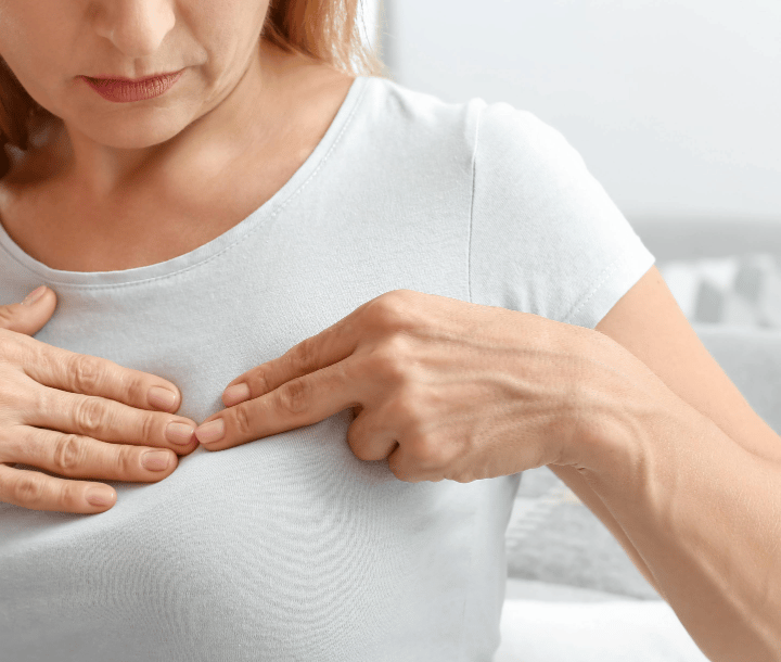 Mujer tocando su pecho con dolor, ilustrando síntomas de mastitis durante la lactancia y la importancia del tratamiento adecuado.