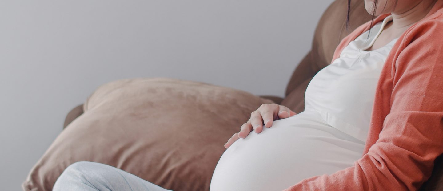 Pregnant Woman Sitting On Couch Holding Belly