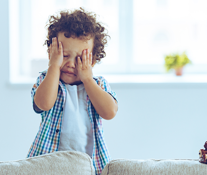 Niño con expresión de cansancio y las manos en la cara, representando síntomas de la anemia infantil.