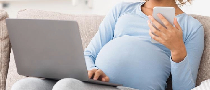 Pregnant woman using laptop and phone to plan 
