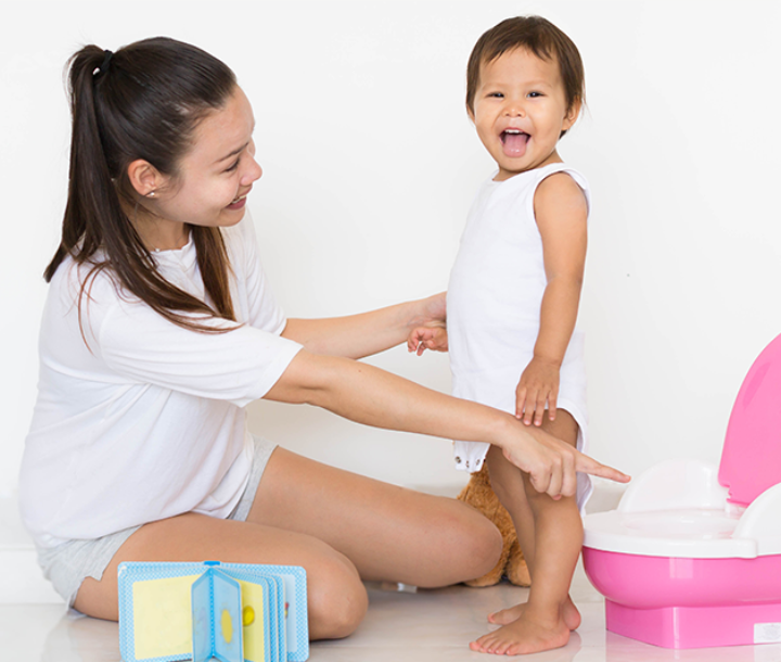 Madre sonriente ayuda a su hijo pequeño en el entrenamiento para dejar el pañal con un inodoro infantil rosa.