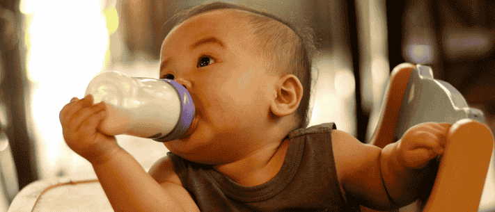 Baby Drinking Milk From A Bottle While Sitting In A High Chair Indoors