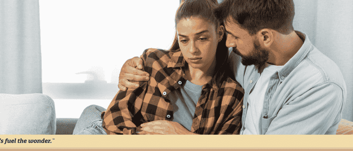 Man Comforting Sad Woman on Sofa with Tagline 'Let's Fuel the Wonder