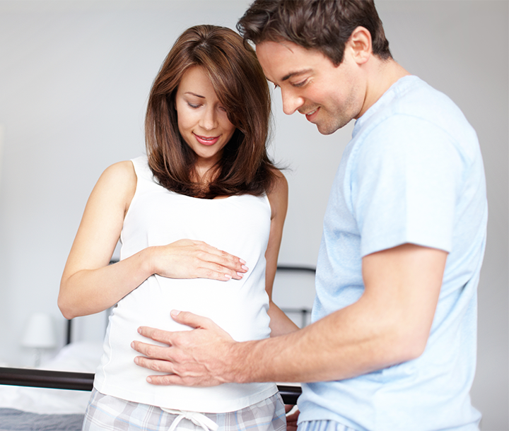 Mujer embarazada acompañada de su pareja en consulta médica, recibiendo orientación sobre la visita al hospital.