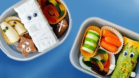Two lunchboxes with cute food art on a blue surface