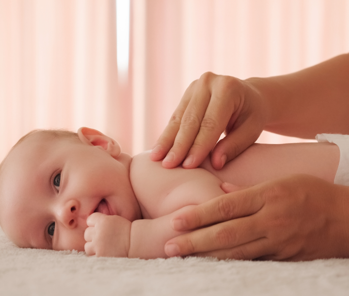 Bebé acostado boca arriba mientras recibe un masaje en el abdomen para aliviar síntomas de cólico.