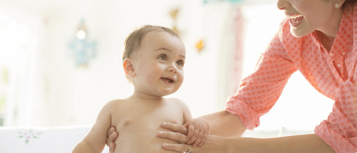 Smiling Mother in Orange Shirt Standing with Her Happy Baby