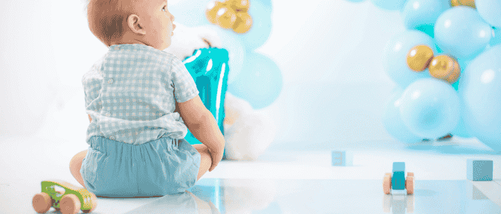 Baby Celebrating First Birthday with Toy Car and Number One Balloon