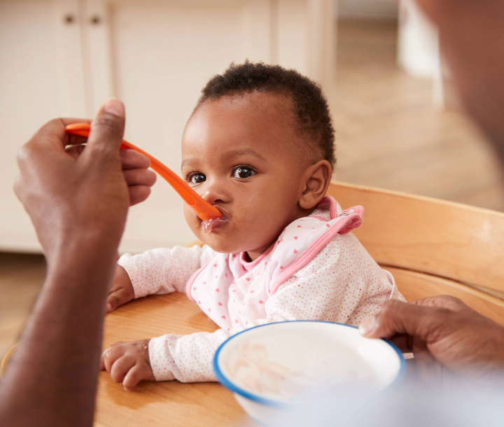 Madre alimentando a su bebé pequeño con cuchara, acompañado de texto sobre la alimentación durante los primeros 6 meses de vida y la importancia de las proteínas completas.