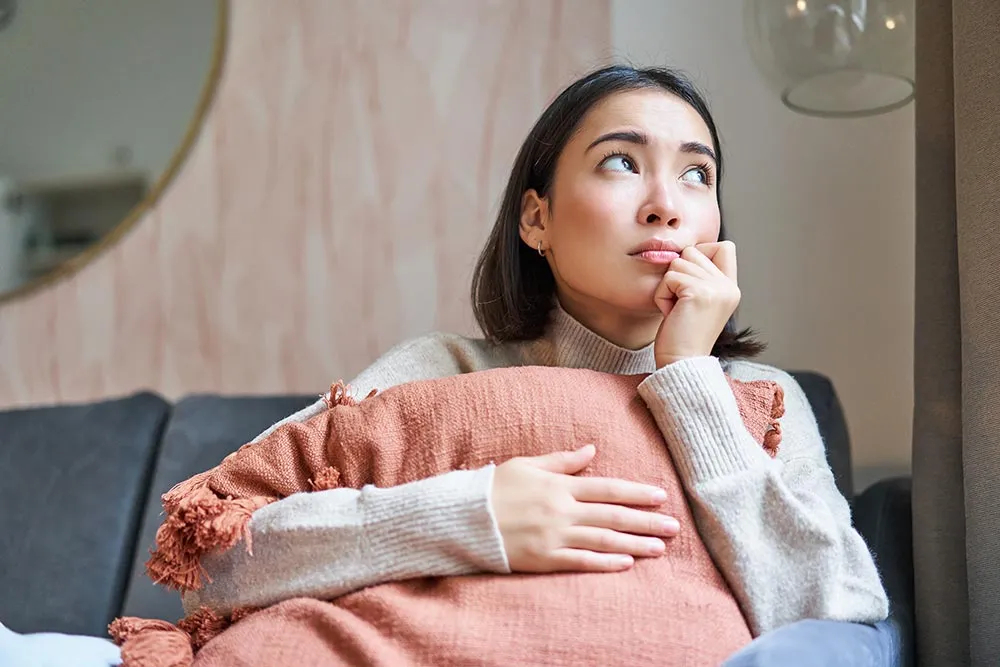 Pregnant woman sitting on couch looking thoughtful while holding a pillow