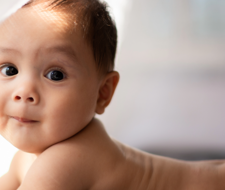 Bebé de once meses acostado sobre la cama y sonriendo mientras juega con su madre, acompañado de texto sobre el mundo del bebé al acercarse a su primer año.