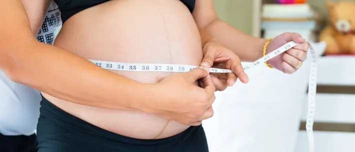 Closeup of husband helping pregnant wife check weight gain with measuring tape