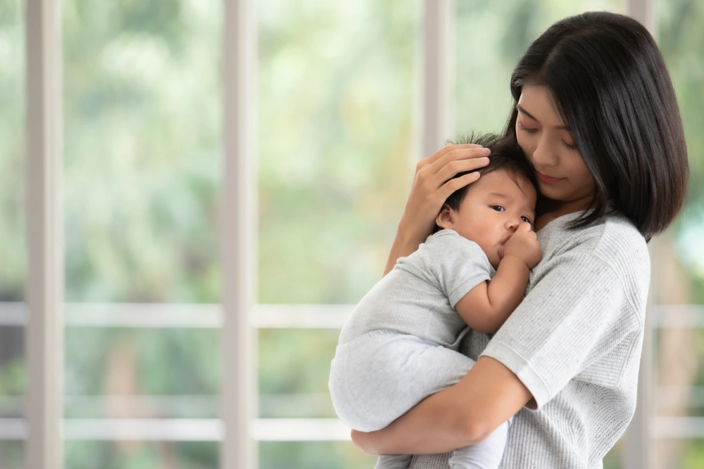 Mother cradling her baby with windows in the background