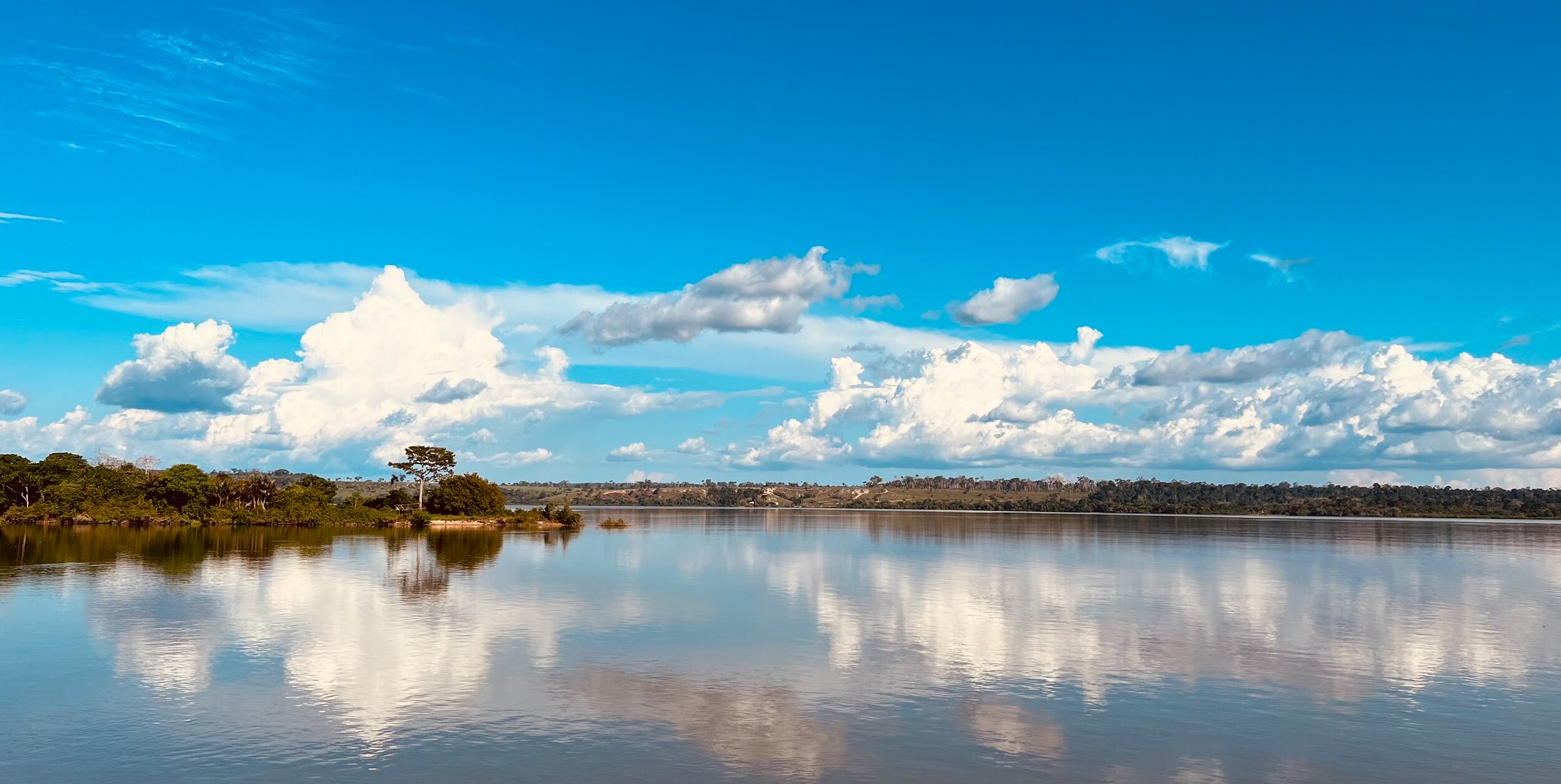 Calm lake reflecting clouds under a bright blue sky