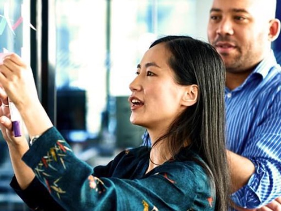 Businesswoman sticking notes on glass with colleague
