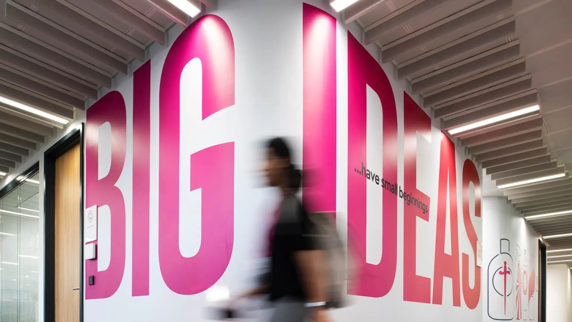 Hallway with large pink wall text reading ‘BIG IDEAS’ and a person walking past.