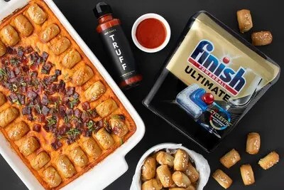 Tray of baked pasta bites with dipping sauce, pretzels, and Finish Ultimate dishwasher detergent packaging