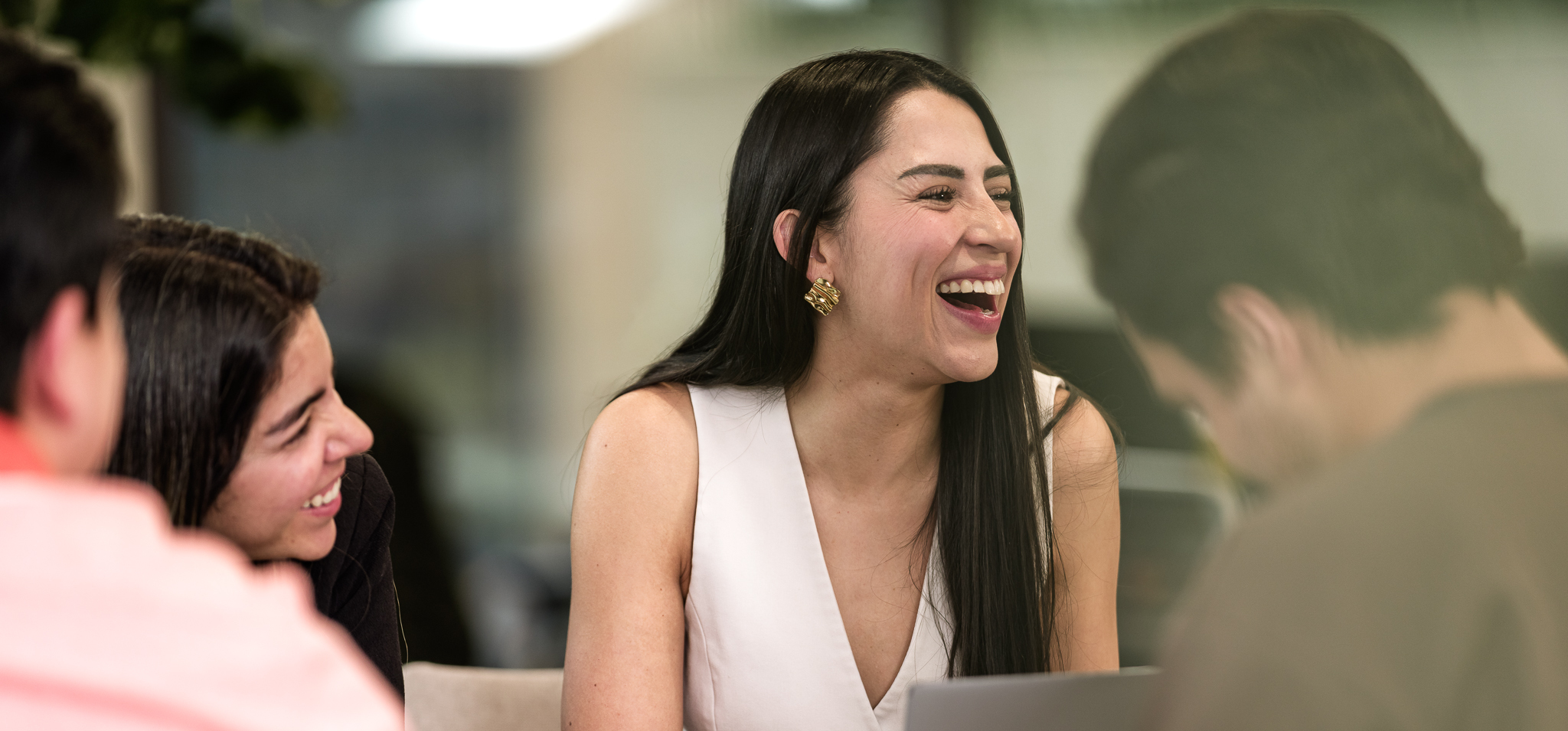 Colleagues smiling and collaborating around a laptop during a team meeting