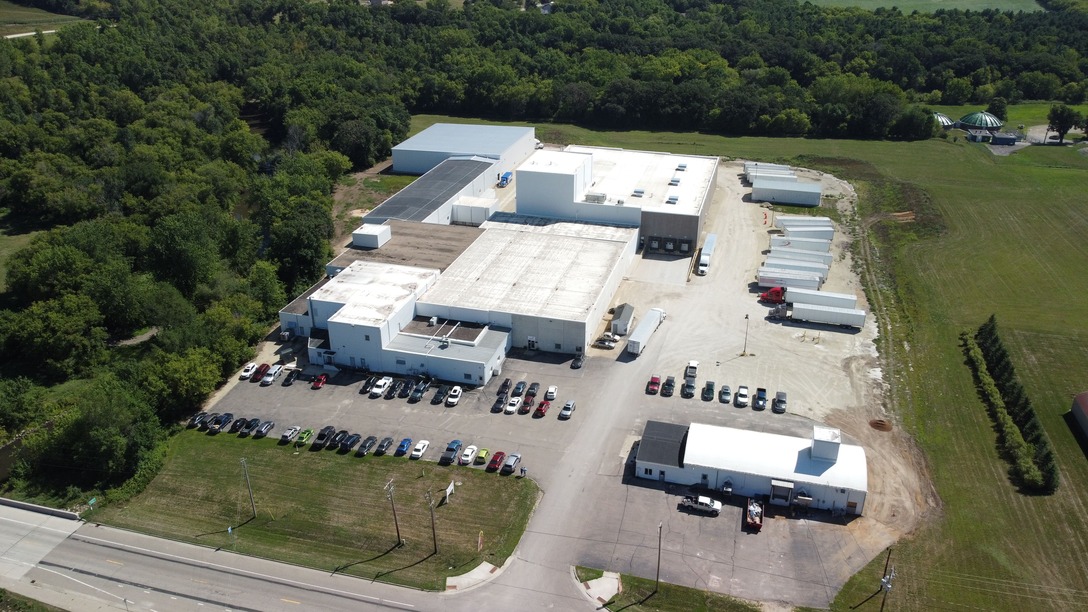 A large modern office complex with landscaped gardens, multiple parking spaces including handicapped spots, and a multi-level parking structure surrounded by greenery.