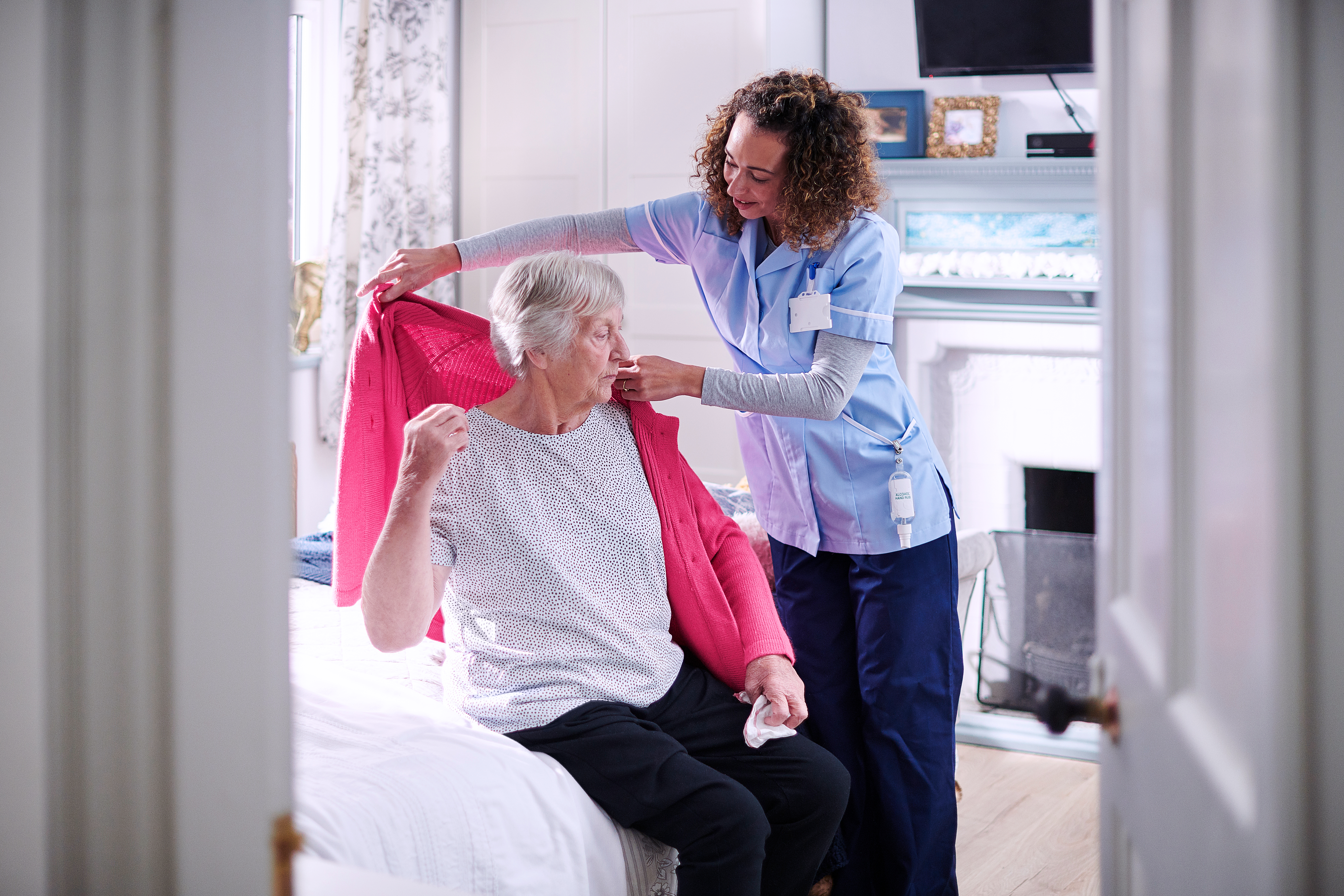 Caregiver helping an elderly woman put on a cardigan