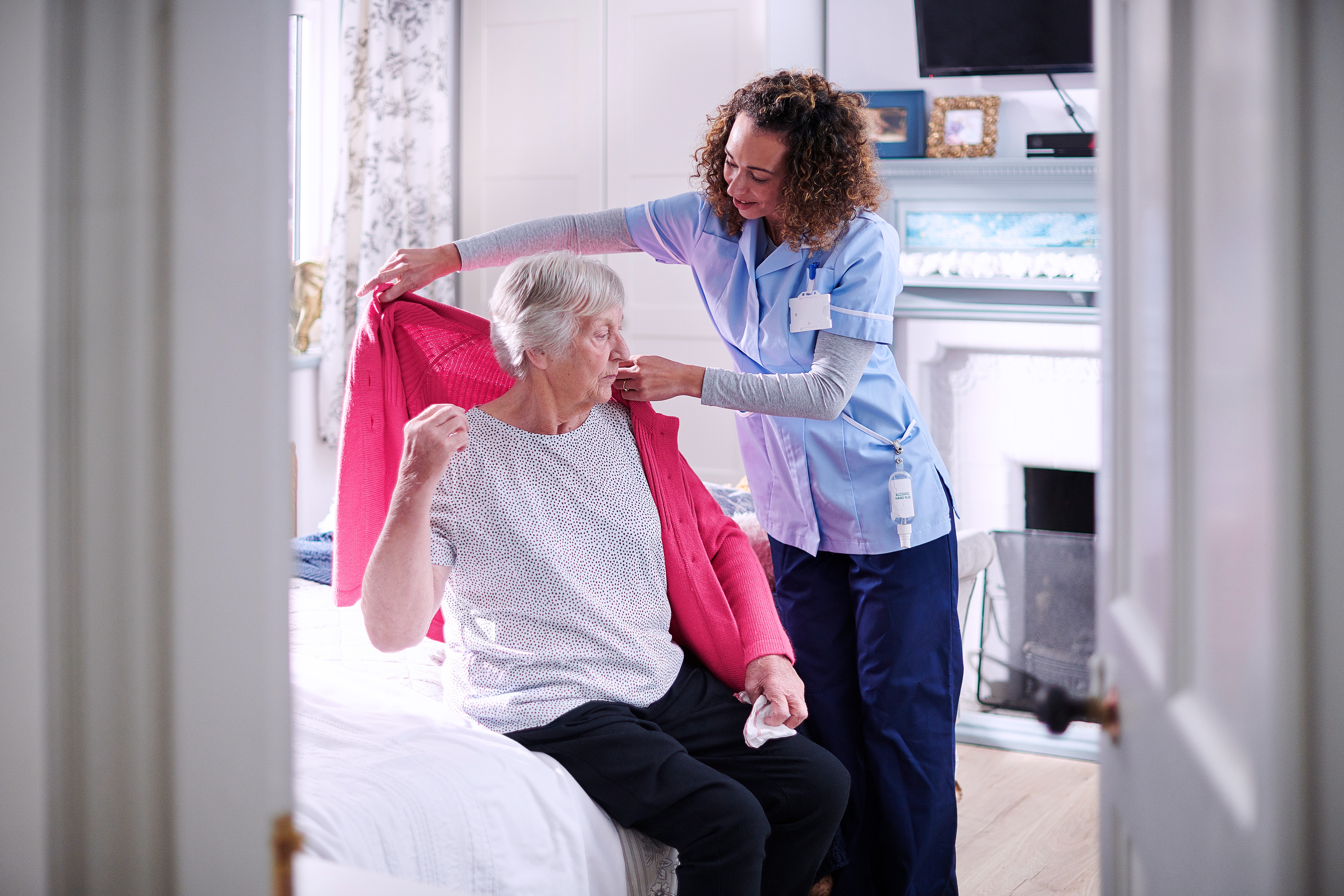 Caregiver helping an elderly woman put on a cardigan
