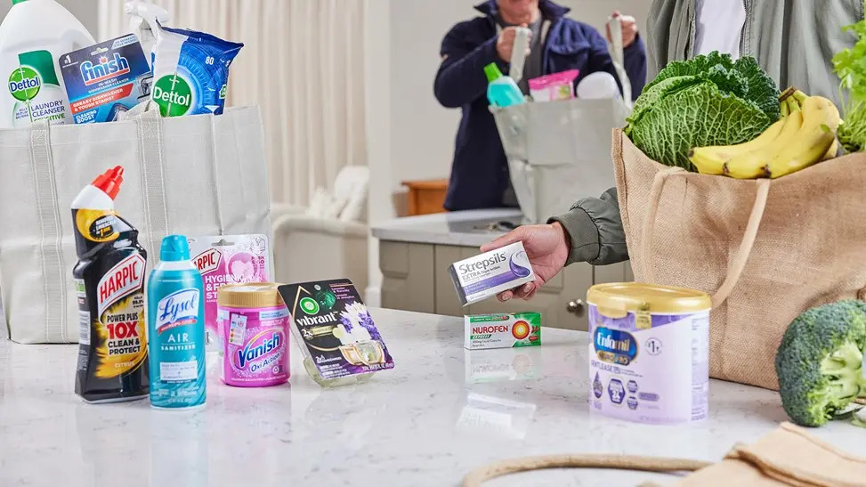 A shopper selecting Reckitt products alongside groceries at a supermarket checkout.